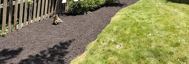 Fence-line landscape bed finished with fresh mulch beside a healthy lawn